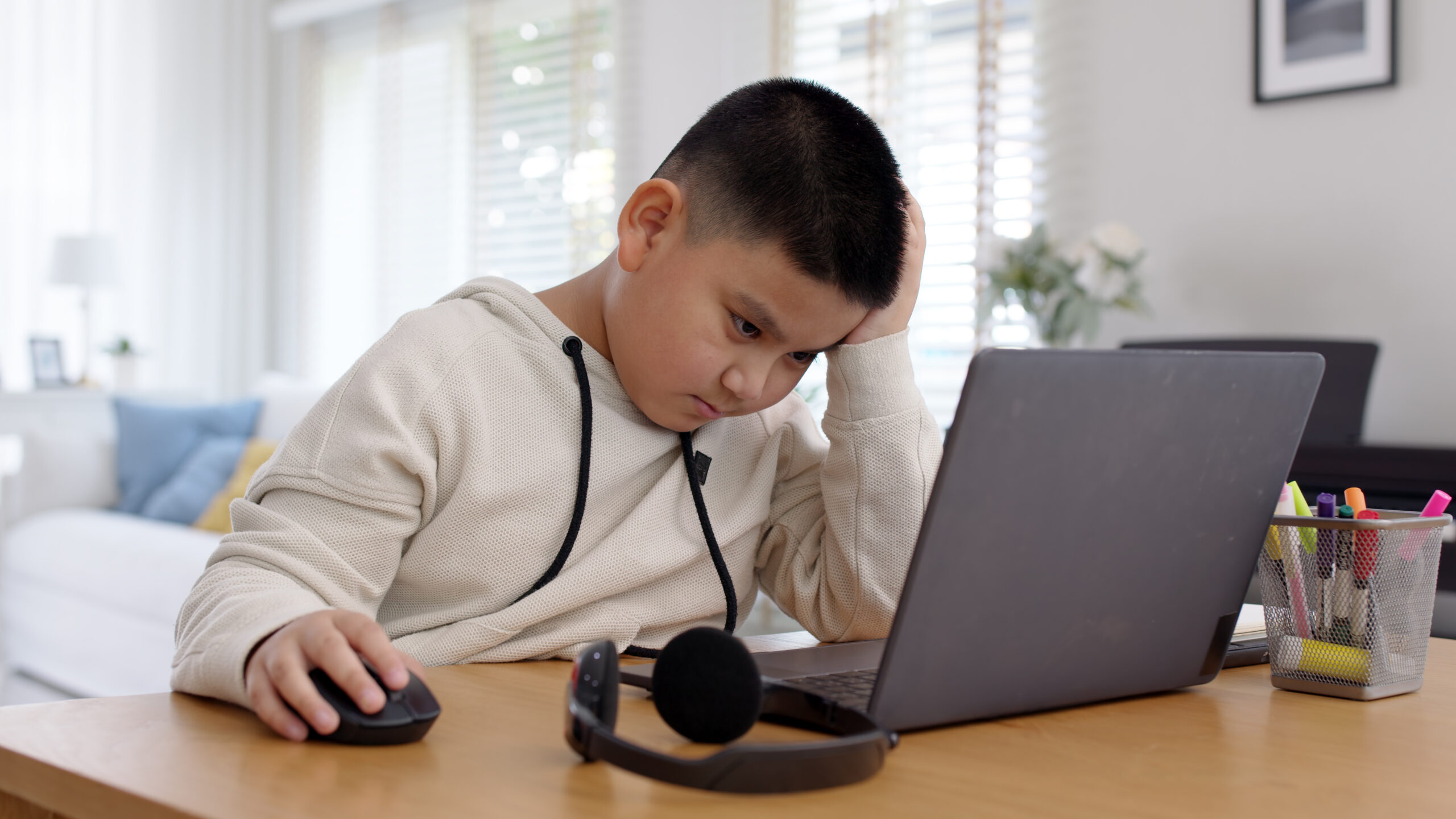 Young asia boy kid sit on desk look at computer notebook feeling bored tired and sleepy in remote learning loss online problem at home distant e-learning primary school class room challenge concept.